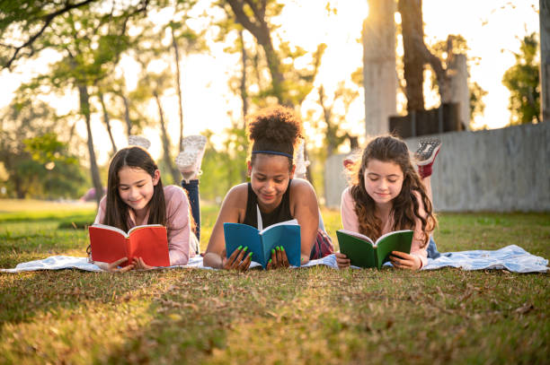 la ragazza della studentessa si sdraia a leggere il libro con il tramonto nel parco della scuola - legge foto e immagini stock