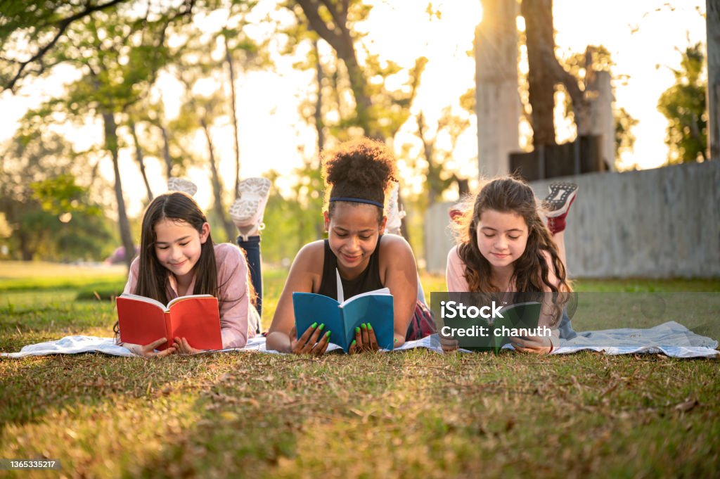 Student girl lie down reading book with sunset in the school park Reading Stock Photo