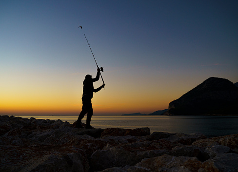 silhouette of a backpack and fishing rod against the rising sun and the sea