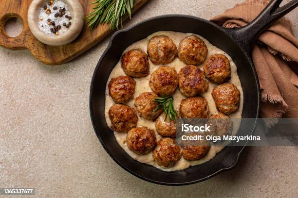 Homemade Swedish Meatballs Made With Ground Meat Onion Egg Bread Crumbs And Nutmeg With Creamy Gravy In Black Pan Skillet On Beige Concrete Table Stock Photo - Download Image Now