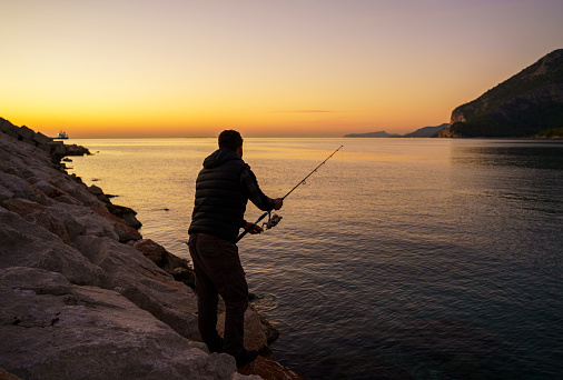 Silhouette of a young man fishing at morning sunrise in Antalya Turkey
