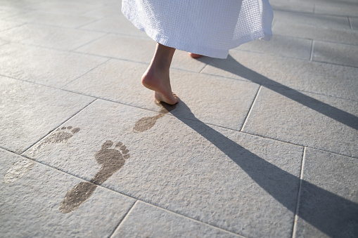 closeup perspective view of feet of child dressed in white bathing robe leaving wet footprints on stone near pool