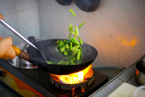 The wok in fire during frying green vegetable at home kitchen.