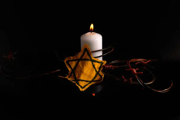 Photo of Holocaust memory day. Arbed wire and burning candle on black background