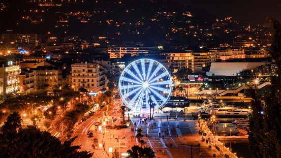 View of Cannes, France at night. Embankment street, ferris wheel, nightlights, moored yachts