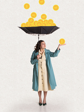 Young woman in retro style attire with umbrella standing under bitcoin rain. Surrealism. Concept of earning, saving and investing money. Crypto currency, business, finance