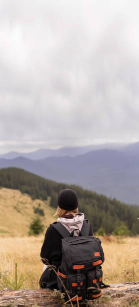 istock A woman with a backpack sitting on the slope on a fallen tree and enjoying the scenic view. Hiking and climbing to the top of the mountain. 1365356733