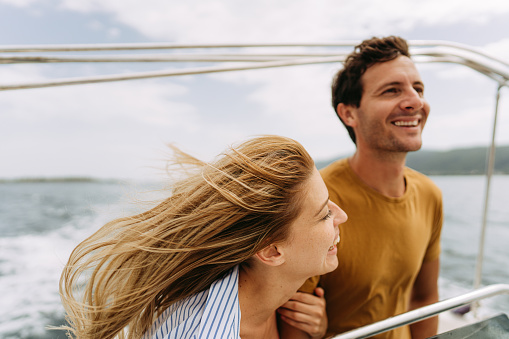 Caucasian romantic couple looking at beautiful view during yachting. Attractive young man and woman hanging out celebrating anniversary honeymoon trip while catamaran boat sailing during summer sunset