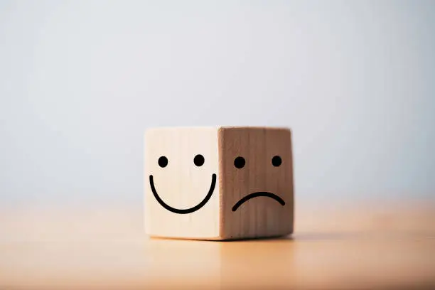 Photo of Smile face in bright side and sad face in dark side on wooden block cube for positive mindset selection concept.