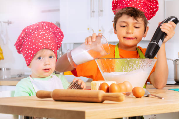 istock Boy add sugar and mix dough in bowl with brother 1365363373