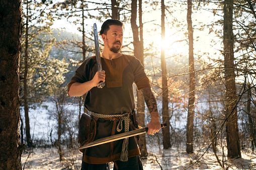 Dedicated mid-adult medieval warrior in the forest during winter, with swords in his hands