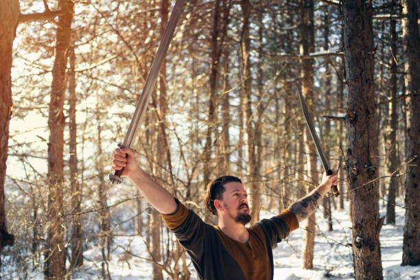Mid-adult medieval warrior celebrating the win at the battle with arms raised while holding the sword