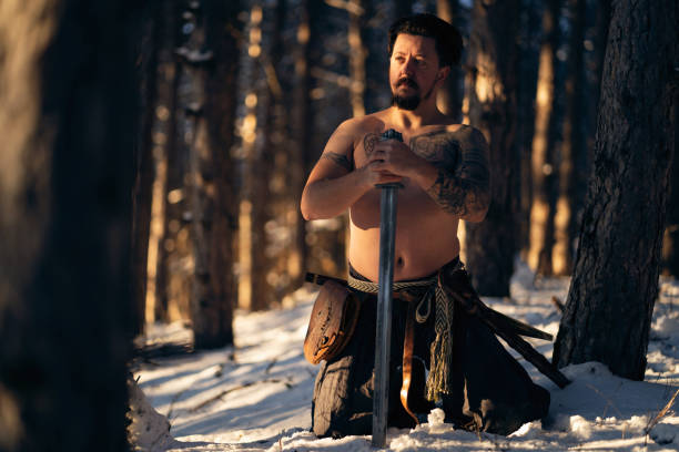 istock Shirtless medieval warrior in the forest, kneeling while praying to his God 1365367623