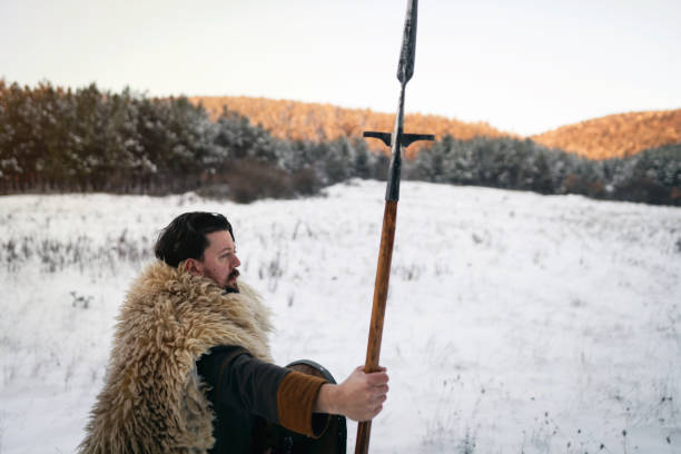 Side view of confident mid-adult Caucasian man, wearing the warrior costume, shield and spear, at nature during winter