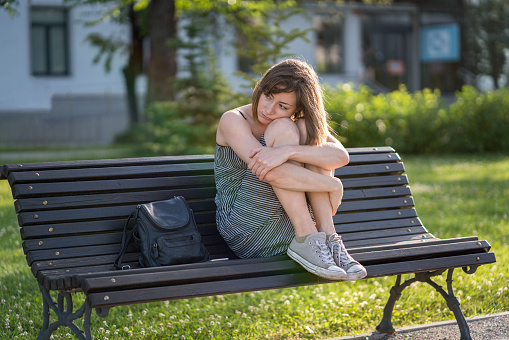 Girl in summer dress and sneakers feeling lonely on a bench