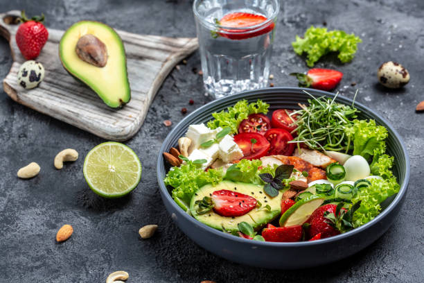 alimentos de dieta keto. keto desayuno pollo a la parrilla y aguacate, queso feta, huevos de codorniz, fresas, nueces y lechuga sobre fondo gris - quail egg almond tomato white meat fotografías e imágenes de stock