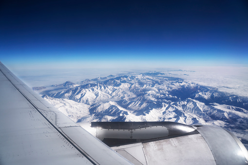 Airplane view of mountains with snow and wing.