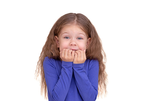 Fearful child kid holding raised fists close to mouth, isolated on white background looking at camera waist up caucasian little girl of 5 years in blue