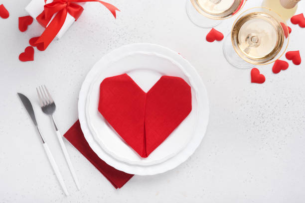 istock Valentinas day table setting white color with white silverware, red napkin folded as heart, candles, champagne, glasses on white background for greetings. Romantic dinner or menu concept. Mock up. 1365379551