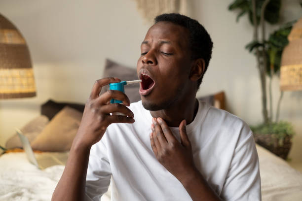 istock Young african man using asthma inhaler sitting at home 1365379814