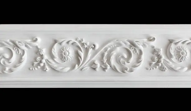 A fragment of a white plaster ceiling molding with an ornament. Isolated on black, close-up