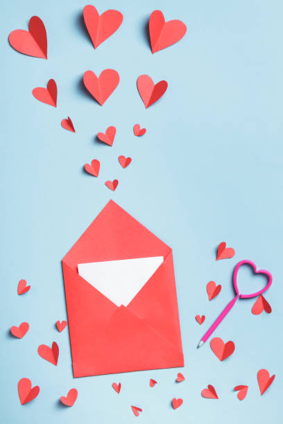 istock Red paper envelope with a white note inside a pen and paper hearts on a blue background. Love letter valentine concept. 1365380779
