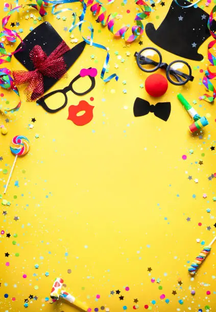 Colorful carnival or birthday party background with streamers, confetti and funny faces formed from bow tie, hat, eyeglasses and lips
