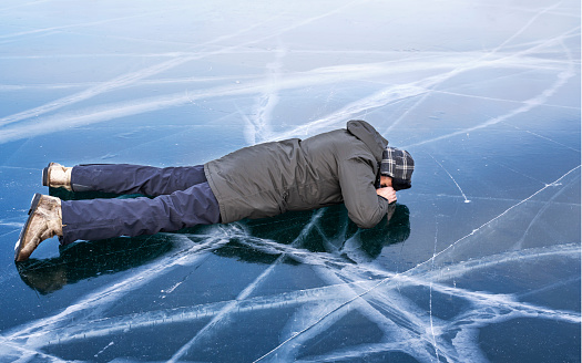 Tourist lies face down on the frozen ice of Lake Baikal. Baikal ice is so clean and transparent that you can see the bottom through it