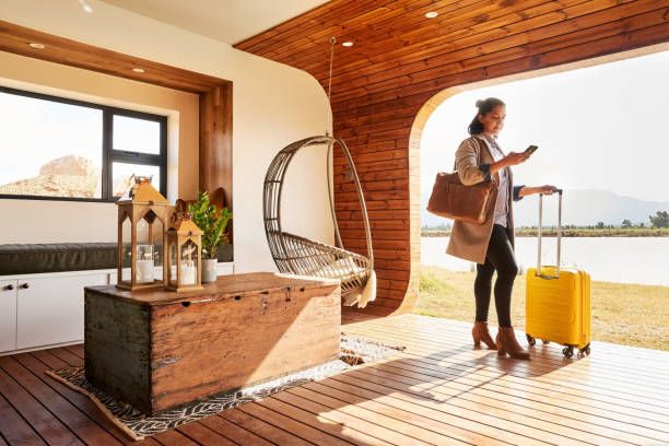 jeune femme avec un bagage utilisant son téléphone dans sa maison de vacances - maison de vacances photos et images de collection