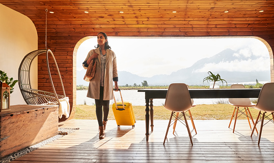 Beautiful young woman with a wheeled suitcase arriving at her vacation rental home