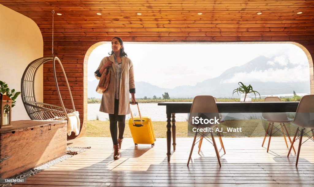 Young woman arriving at a holiday home resort for her vacation Beautiful young woman with a wheeled suitcase arriving at her vacation rental home Luxury Stock Photo