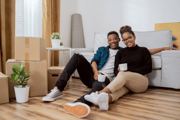 Smiling couple sitting on the floor relaxing after moving in, drinking coffee in their new apartment, around them boxes with unpacked things, the husband embraces his wife Smiling couple sitting on the floor relaxing after moving in, drinking coffee in their new apartment, around them boxes with unpacked things, the husband embraces his wife tenant stock pictures, royalty-free photos & images