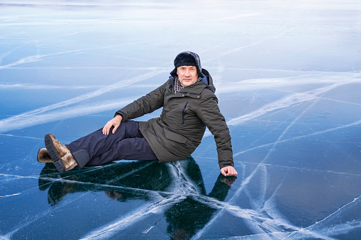 Tourist sits on the frozen ice of Lake Baikal. Baikal ice is so clear and transparent that the bottom can be seen through it
