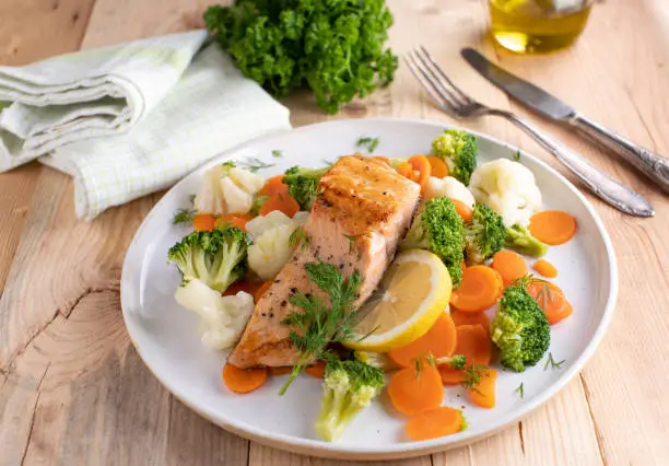 Fresh and homemade low carb or ketogenic meal for dieting with roasted salmon fillet served with buttered imperial vegetables on plate with lemon