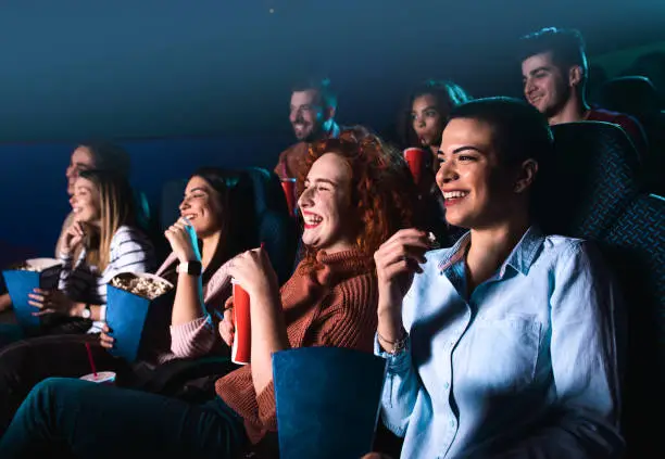 Photo of Group of cheerful people laughing while watching movie in cinema.