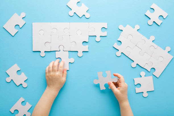 istock Baby boy hands playing and putting together white puzzle pieces on light blue table background. Pastel color. Closeup. Point of view shot. Children development. Top down view. 1365388024