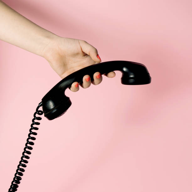 istock Artistic visual with female hand holding bold black phone receiver. Vintage ambient on pastel background. Minimal composition. 1365394908
