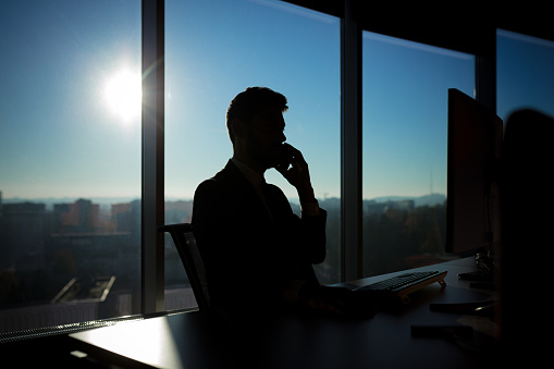 Successful businessman boss working at computer on the background of large windows, silhouette