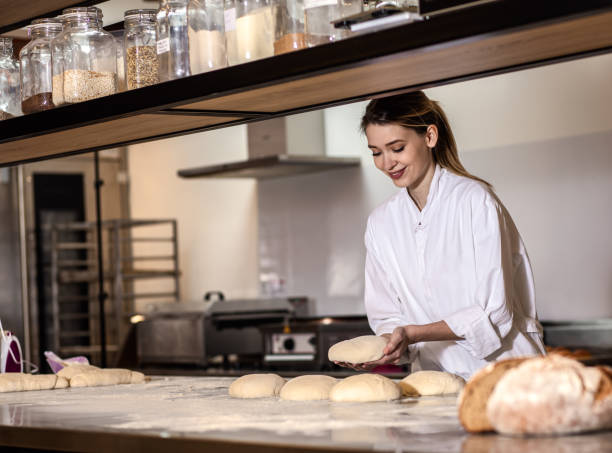 istock Young female baker preparing dough for bread in modern manufacturing. 1365400198