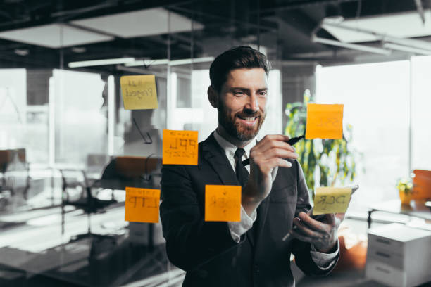 istock Successful businessman rewrites a task on a glass board with colored stickers, from phone and tablet 1365400220
