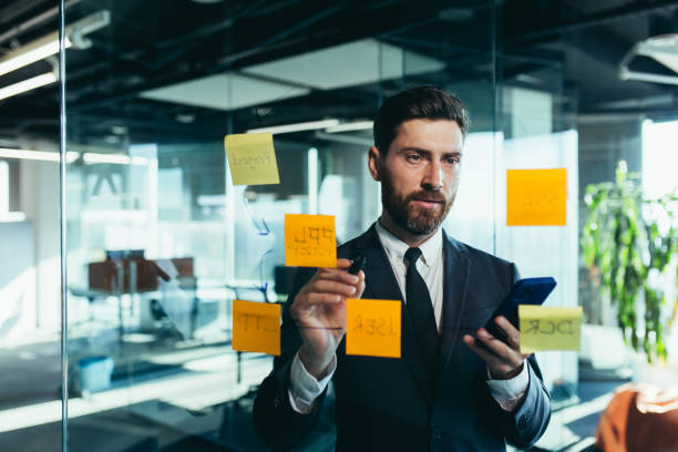 istock Successful businessman rewrites a task on a glass board with colored stickers, from phone and tablet 1365400234