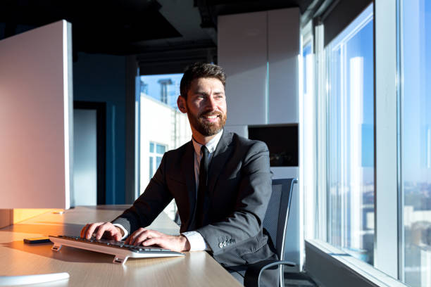 istock Happy successful businessman with a beard working at a computer in a modern office, smiling and rejoicing, confident boss 1365400351