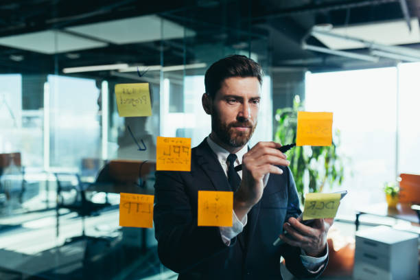 istock Successful businessman rewrites a task on a glass board with colored stickers, from phone and tablet 1365400472