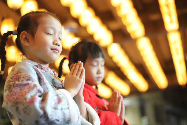due gemelle asiatiche che indossano il cheongsam fanno una visita di capodanno sotto le lanterne davanti a un tempio. - 6 7 years little girls child portrait foto e immagini stock