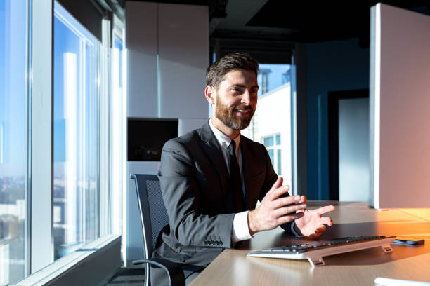 istock Businessman with a beard working in the office, a man talking on a video call, looking at the webcam, and talking, having fun gesturing with his hands 1365401150