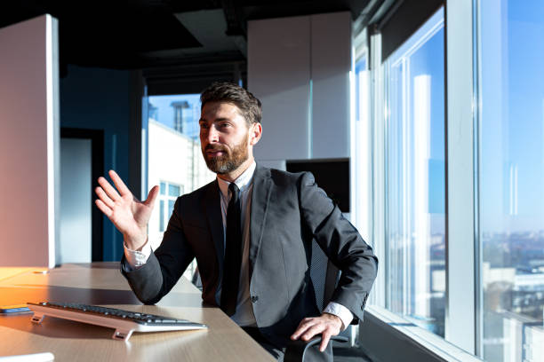 istock Businessman with a beard working in the office, a man talking on a video call, looking at the webcam, and talking, having fun gesturing with his hands 1365401251