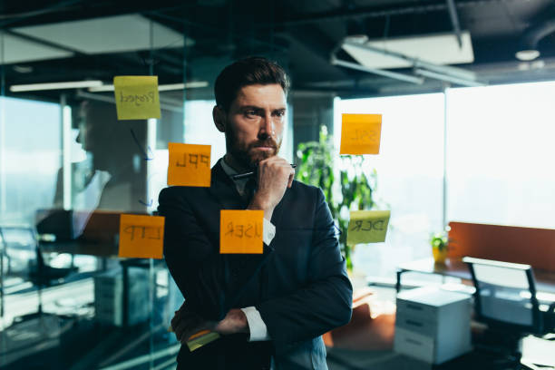istock businessman in reflection at a glass task board, hangs plans on colored paper stickers, plans for the near future 1365401352