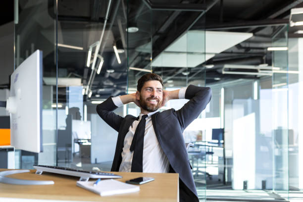 istock Happy and dreamy businessman, resting at work with his hands behind his head, working in a modern office at the computer 1365402203