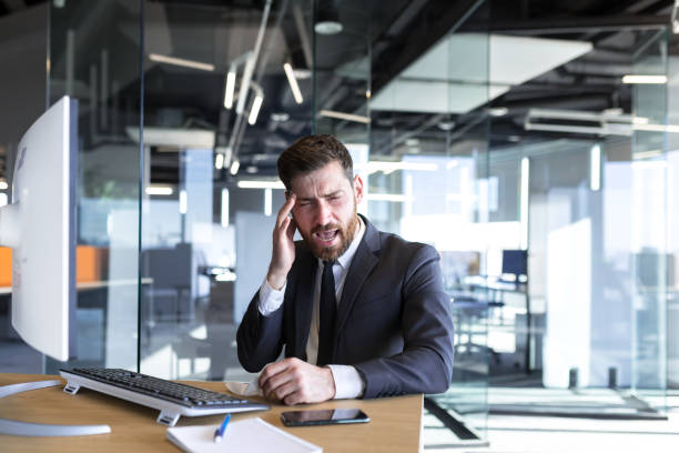 istock Businessman working in the office at a desk with a computer, a tired man has a severe headache 1365402289