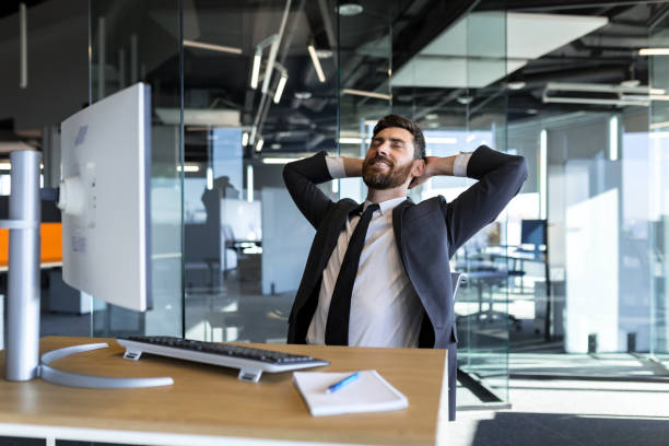 istock Happy and dreamy businessman, resting at work with his hands behind his head, working in a modern office at the computer 1365402406